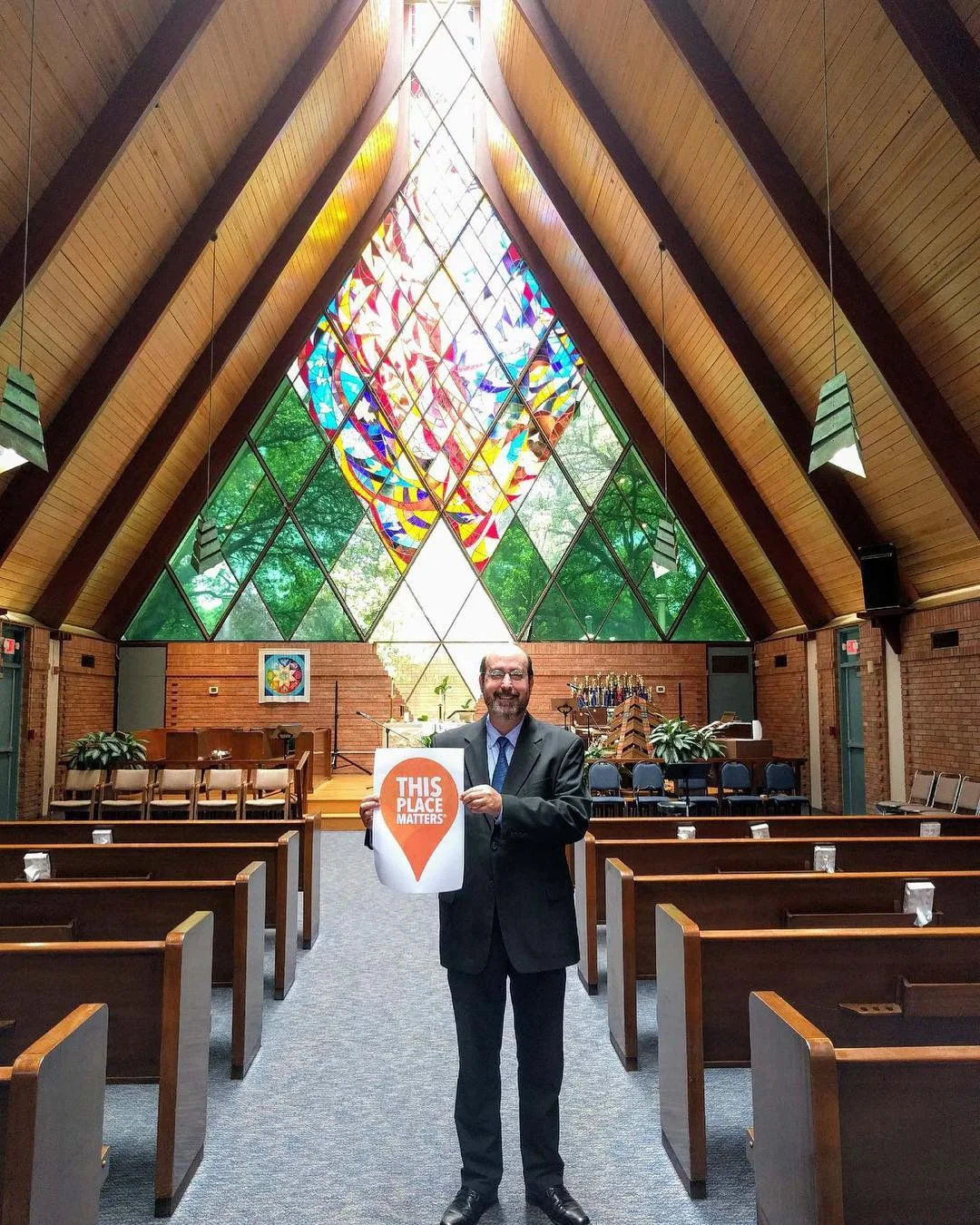 Mid Tex Mod advocate holding a This Place Matters sign inside a mid-century modern A-frame church with diamond-patterned stained glass
